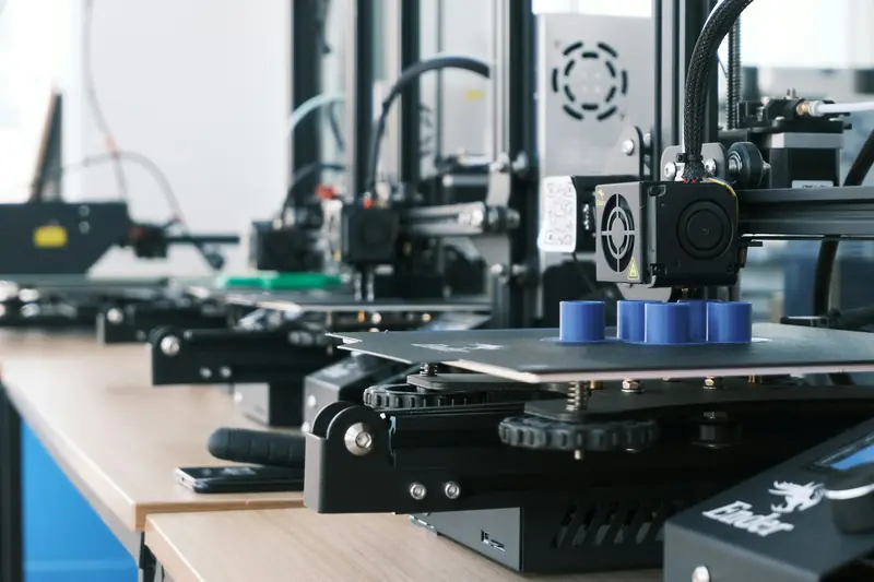Fila di stampanti 3D FDM che stampano cilindri blu